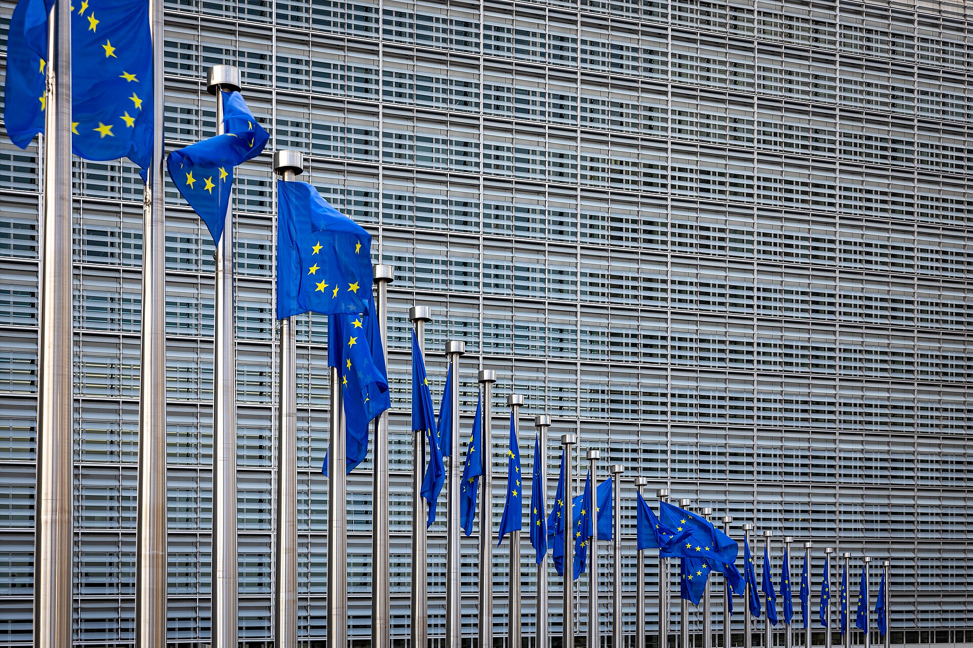 Rows of blue European Union flags flying in front of the glass facade of the Berlaymont building in Brussels