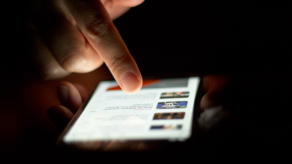 Close-up of a finger scrolling through content on an illuminated smartphone against a dark background